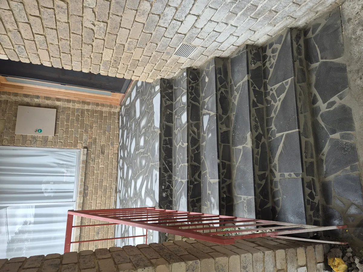 Outdoor stairs and landing area with irregular dark gray mosaic tile pattern, brick walls and red metal railing in Melbourne