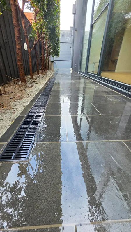 Finished bluestone side path washed down, with a grated drainage channel along the fence
