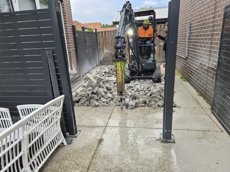 Mini excavator with hydraulic breaker removing an old concrete path in a Melbourne side yard