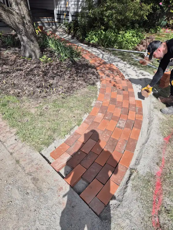 Tradesman laying a curved red brick garden path in Melbourne