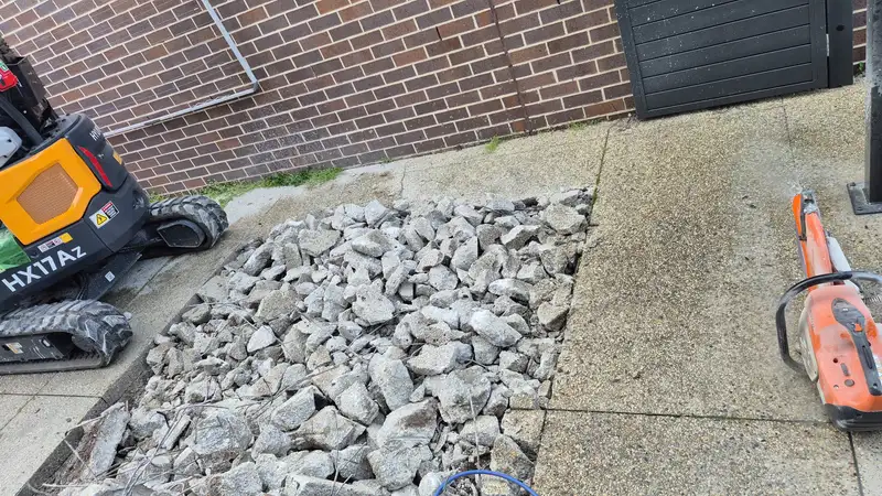 Broken concrete rubble next to a mini excavator ready for removal