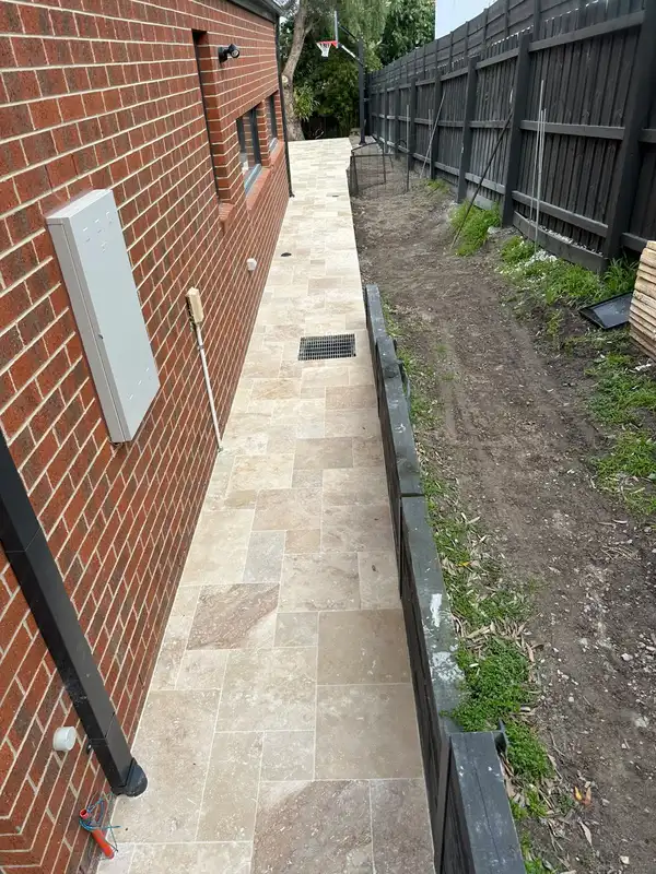 Travertine pathway along a red brick house wall